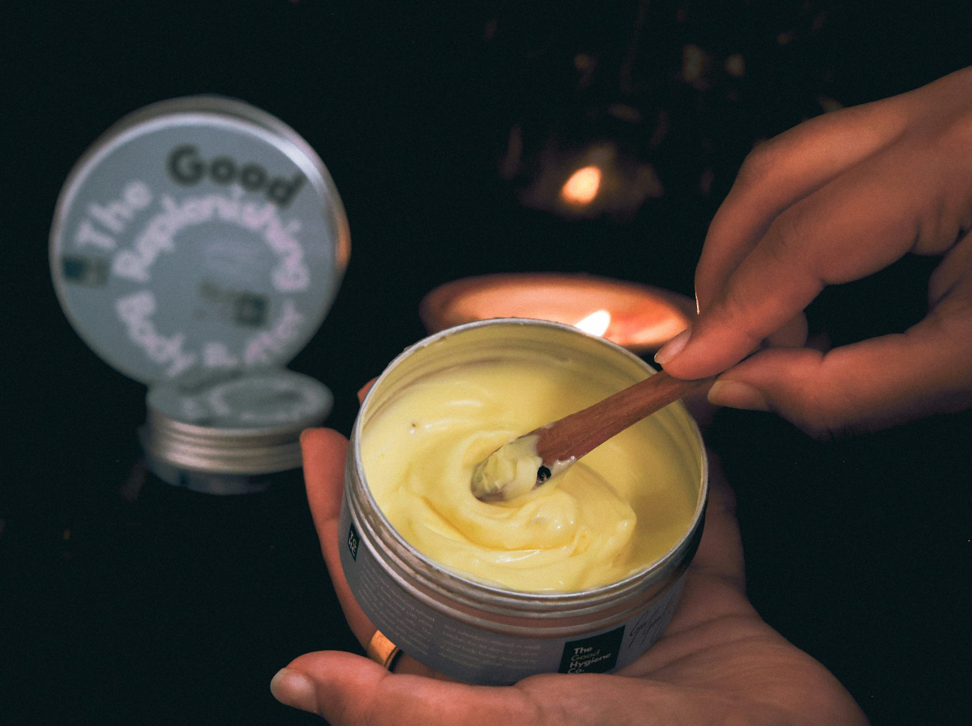 Hands scooping creamy body butter from tin